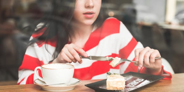 mulher-de-blusa-listrada-comendo-uma-sobremesa-com-café-exemplo-de-ação-contínua-acontecendo-gerúndio